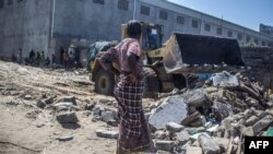 Une femme regarde un bulldozer qui enlève les décombres de sa maison démolie à Xwlacodji, dans le 5ème arrondissement de Cotonou, le 3 septembre 2019, après le passage des bulldozers.