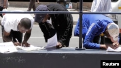 FILE - Zimbabweans fill out application forms outside Immigration offices in Johannesburg.