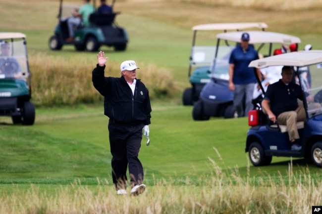 El presidente de EE.UU., Donald Trump, saluda a los manifestantes mientras juegan al golf en el club de golf Turnberry, en Turnberry, Escocia, el sábado 14 de julio de 2018.