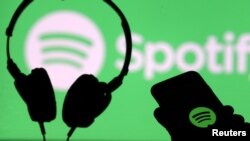 Unos auriculares y un teléfono inteligente frente a una pantalla con el logotipo de Spotify. [Foto de archivo]