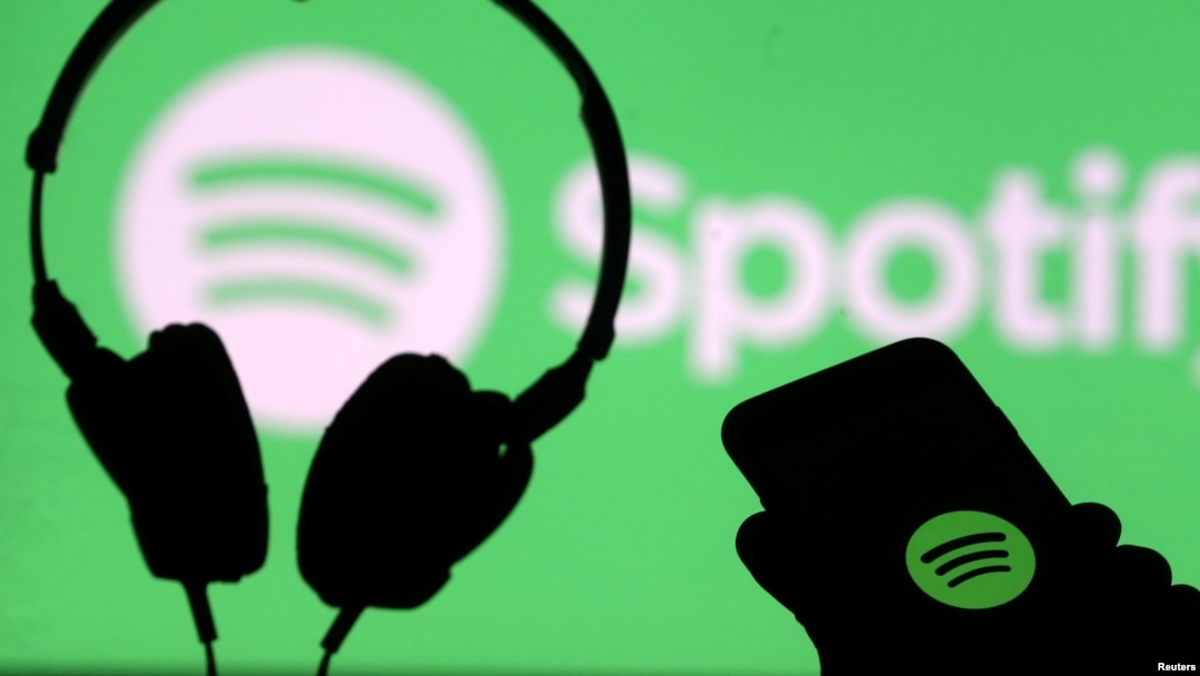 Unos auriculares y un teléfono inteligente frente a una pantalla con el logotipo de Spotify. [Foto de archivo]