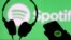 Unos auriculares y un teléfono inteligente frente a una pantalla con el logotipo de Spotify. [Foto de archivo]