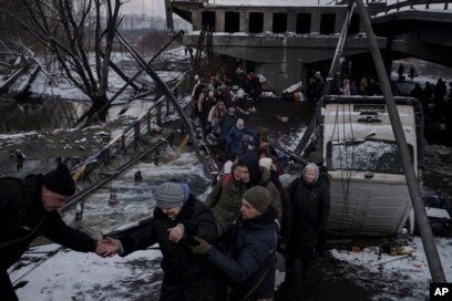 Warga Ukraina melintasi jalur improvisasi di bawah jembatan yang hancur saat melarikan diri dari Irpin, di pinggiran Kyiv, Ukraina, Selasa, 8 Maret 2022. (Foto: AP)