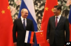 Bendera nasional Rusia dan China berdiri di latar depan saat Presiden Rusia Vladimir Putin, kiri, dan mitranya dari China Xi Jinping berdiri bersama. (Foto: AP)