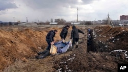 Ljudi vuku mrtvo telo ubijenog čoveka ka zajedničkoj grobnici, pošto su pojedinačne sahrane nemoguće usled teškog bombardovanja koje ruske snage izvode na grad Mariupolj, u Mariupolju, 9. marta 2022.