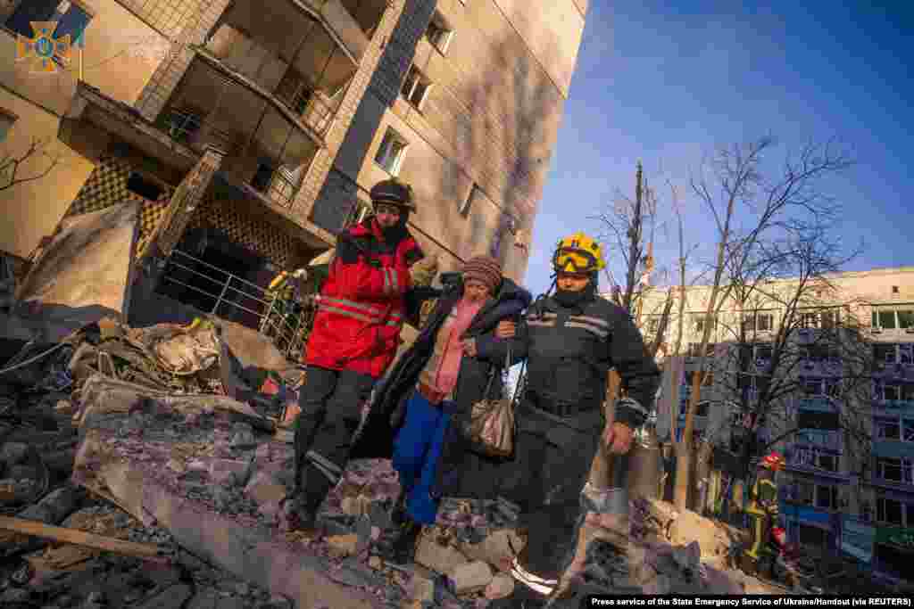 Rescuers help a woman evacuate a residential building damaged by shelling in Kyiv in this handout picture released March 16, 2022.