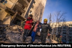 Tim penyelamat mengevakuasi seorang perempuan dengan latar belakang sebuah bangunan tempat tinggal yang rusak akibat penembakan, saat serangan Rusia di Ukraina berlanjut, di Kyiv, Ukraina, 16 Maret 2022. (Foto: via Reuters)