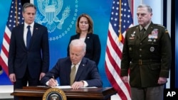President Joe Biden signs a bill for more assistance to Ukraine, on the White House campus in Washington, March 16, 2022, as Secretary of State Antony Blinken, Deputy Secretary of Defense Kathleen Hicks and Chairman of the Joint Chief of Staff General Mark Milley look on.