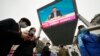 People walk past a large video screen at a shopping mall showing Chinese Premier Li Keqiang as he speaks during a press conference after the closing session of China's National People's Congress (NPC) in Beijing, March 11, 2022.