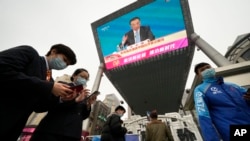 People walk past a large video screen at a shopping mall showing Chinese Premier Li Keqiang as he speaks during a press conference after the closing session of China's National People's Congress (NPC) in Beijing, March 11, 2022.