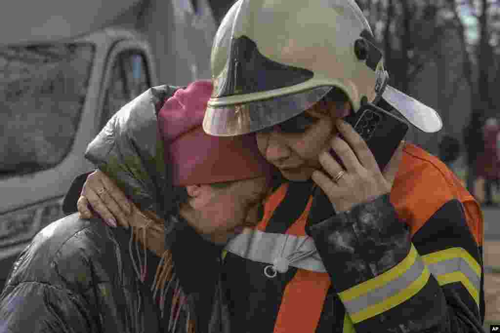 A firefighter comforts a woman outside a destroyed apartment building after a bombing in a residential area in Kyiv, March 15, 2022.