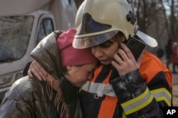 A firefighter comforts a woman outside a destroyed apartment building after a bombing in a residential area in Kyiv, Ukraine, March 15, 2022. (AP Photo/Vadim Ghirda)