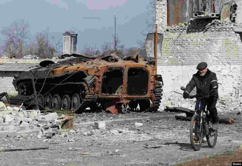 A local resident rides a bicycle past a charred armored vehicle in the separatist-controlled town of Volnovakha in the Donetsk region, Ukraine, March 15, 2022.