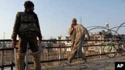 A Kashmiri civilian walks past an Indian policeman standing near a barbed wire during curfew in Srinagar, India, February 9, 2013.