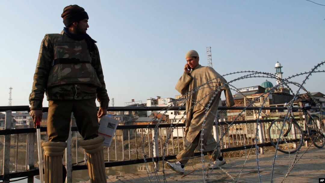 Seorang warga sipil Kashmir berjalan melewati seorang polisi India yang berjaga di dekat pagar berduri saat diberlakukannya jam malam di wilayah Srinagar, India, 9 February 2013. (AP Photo/Mukhtar Khan). Seorang warga Kashmir yang divonis bersalah atas perannya dalam serangan terhadap parlemen India tahun 2001, Afzal Guru, telah dihukum gantung di sebuah penjara India, Sabtu (9/2).