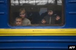 Children look out from a carriage window as a train prepares to depart from a station in Lviv, western Ukraine, enroute to the town of Uzhhorod near the border with Slovakia, on March 3, 2022. - Russian forces have taken over the Ukrainian city of Kherson, local officials confirmed March 2, 2022 the first major urban centre to fall since Moscow invaded a week ago. (Photo by Daniel LEAL / AFP)