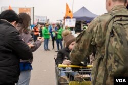 Los soldados polacos ayudan a los refugiados sobrecargados a subir a los autobuses utilizando carros de supermercados para el equipaje y niños pequeños dejándose caer en la parte superior. [Jamie Dettmer/VOA]