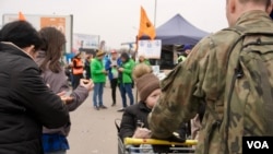 Polish soldiers help over-burdened refugees towards buses using supermarket chariots for luggage and small kids plopped on top. (Jamie Dettmer/VOA)