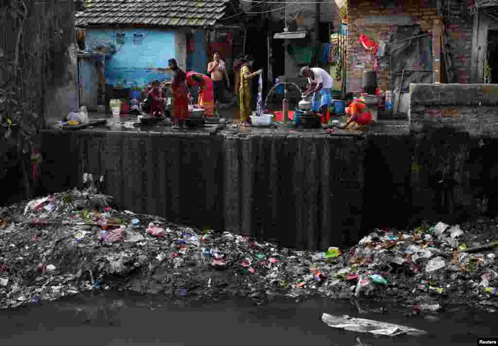 Residents fill water containers and wash their clothes from municipal water pipes alongside a polluted water channel at a slum in Kolkata, India.