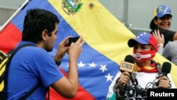 Un hombre toma una foto de una mujer mientras usa una mordaza y una cadena, y sostiene micrófonos durante una manifestación para conmemorar el Día Mundial de la Libertad de Prensa en Caracas, Venezuela, el 3 de mayo de 2016.