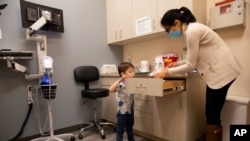 FILE - Hudson Diener, 3, peeks into a cabinet during an appointment for a Moderna COVID-19 vaccine trial in Commack, N.Y., Nov. 30, 2021.