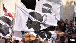 Mourners hold the 'A bandera testa mora', the flag of Corsica, as pallbearers carry the coffin of Corsican nationalist and convicted killer Yvan Colonna ahead of his funeral ceremony in Cargese, Corsica, on March 25, 2022. - 