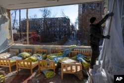 A man removes a destroyed curtain inside a school damaged among other residential buildings in Kyiv, Ukraine, March 18, 2022. Russian forces pressed their assault on Ukrainian cities Friday, with new missile strikes and shelling near Kyiv and Lviv.