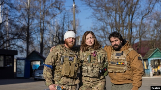 Red Taylor, Alexis Antilla dhe Rob, anëtarë të një grupi vullnetarësh amerikanë pozojnë përpara një spitali në Brovary, pranë Kievit (20 mars 2022)