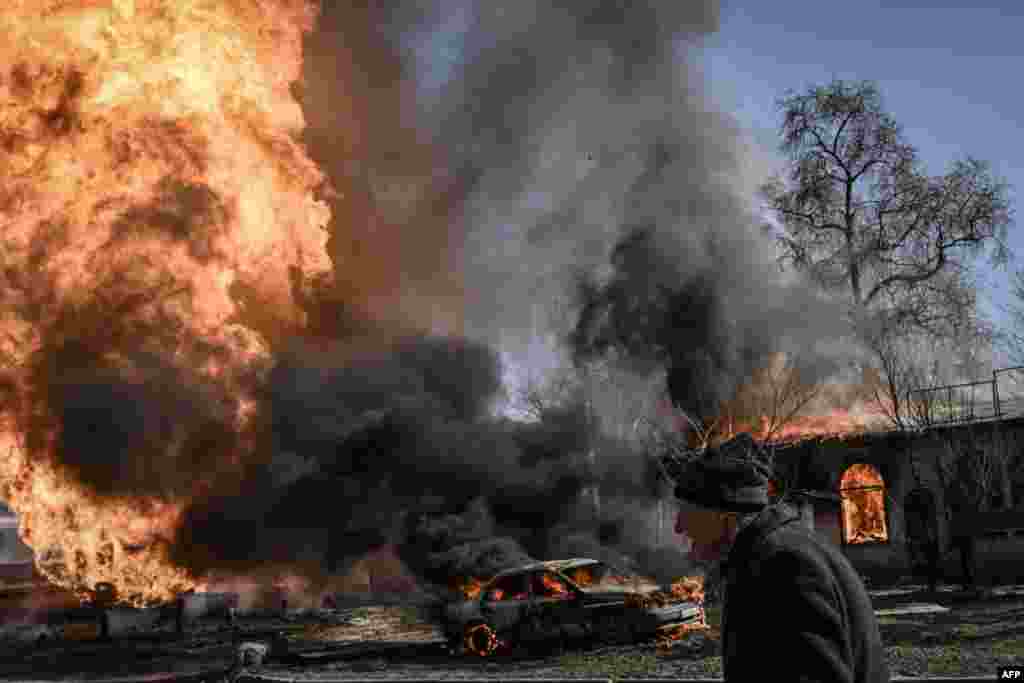 A Ukrainian woman walks past flames and smoke rising coming after shelling took place on the 30th day of the invasion of Ukraine by Russian forces in the city of Kharkiv. (Photo by Aris Messinis / AFP)