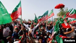 পাকিস্তানের প্রধানমন্ত্রী ইমরান খান ইসলামাবাদে পাকিস্তান তেহরিক-ই-ইনসাফ (পিটিআই) দলের একটি জনসভায় যোগ দিতে হেলিকপ্টার থেকে অবতরণ করার সময় তার সমর্থকেরা পতাকা নেড়ে তাকে স্বাগত জানান। মার্চ ২৭, ২০২২। 