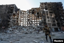 A service member of pro-Russian troops walks near an apartment building destroyed in the course of Ukraine-Russia conflict in the besieged southern port city of Mariupol, Ukraine, March 28, 2022.