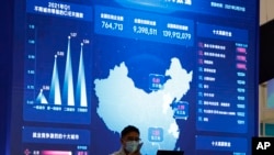 FILE - A man speaks on his phone near a giant display showing big data and a map of China at an internet fair in Beijing, April 30, 2021.