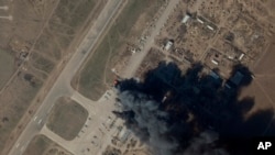 In this satellite picture provided by Planet Labs PBC, fire and smoke is seen at Kherson International Airport and Air Base in Kherson, March 15, 2022. A suspected Ukrainian strike on the air base damaged Russian helicopters and vehicles Tuesday.
