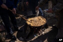 Sukarelawan memasak di halaman sebuah teater di kota Drohobych, Ukraina barat, Senin, 21 Maret 2022. Teater tersebut menjadi titik pertemuan para seniman, termasuk mereka yang mengungsi dari bagian lain Ukraina, untuk membuat makanan bagi tentara dan warga lainnya. (Foto AP / Bernat Armangue)