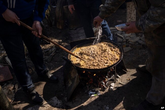 Sukarelawan memasak di halaman sebuah teater di kota Drohobych, Ukraina barat, Senin, 21 Maret 2022. Teater tersebut menjadi titik pertemuan para seniman, termasuk mereka yang mengungsi dari bagian lain Ukraina, untuk membuat makanan bagi tentara dan warga lainnya. (Foto AP / Bernat Armangue)