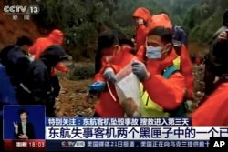 Seorang pekerja darurat memasukkan perekam "kotak hitam" berwarna oranye ke dalam kantong plastik di lokasi kecelakaan penerbangan China Eastern Rabu, 23 Maret 2022, di Kabupaten Tengxian di Guangxi China selatan. Daerah Otonomi Zhuang. (CCTV via AP Video)