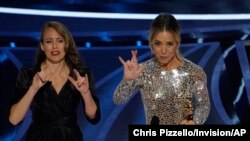 Sian Heder, right, signs "I really love you" as she accepts the award for best adapted screenplay for "CODA" at the Oscars on Sunday, March 27, 2022.