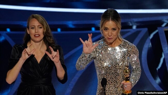 Sian Heder, right, signs "I really love you" as she accepts the award for best adapted screenplay for "CODA" at the Oscars on Sunday, March 27, 2022.