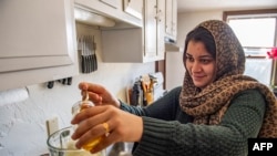 Afghani evacuees Israr, 26, and his wife Sayeda, 23, (pouring in honey) make a morning smoothie of fruit, nuts and milk, an American concept her and her husband Israr have been trying for a few weeks instead of tea, at their new apartment in Charlestown, Massachusetts on February 21, 2022.