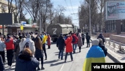 Demonstrators, some displaying Ukrainian flags, chant 'go home' while Russian military vehicles reverse course on the road, at a pro-Ukraine rally amid Russia's invasion, in Kherson, March 20, 2022 in this still image from video obtained by Reuters.