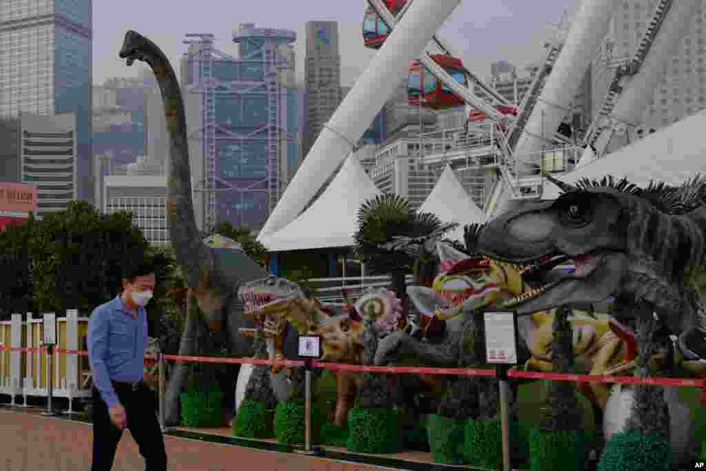 A man wearing a face covering walks past some dinosaur models in the Central district in Hong Kong.