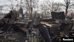 A Ukrainian soldier walks past the remains of a Russian tank in the village of Lukyanova, outside kyiv, as the Russian invasion of Ukraine continues, on March 27, 2022.