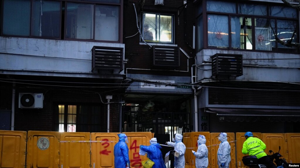 3月25日，身穿防护服的医务人员在上海一座被封闭小区的临时护墙外进行检查。(photo:VOA)