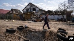 A man walks behind a crater created by a bomb and in front of damaged houses following a Russian bombing earlier this week, outskirts Mykolaiv, Ukraine, March 25, 2022.