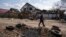 A man walks behind a crater created by a bomb and in front of damaged houses following a Russian bombing earlier this week, outskirts Mykolaiv, Ukraine, March 25, 2022.