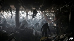 Ukrainian firefighters and servicemen search for people under debris inside a shopping center after a bombing in Kyiv, Ukraine, March 21, 2022. 