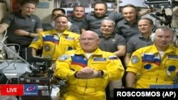 ইউক্রেনের পতাকার রঙে নীল স্ট্রাইপযুক্ত হলুদ স্যুট পরা রাশিয়ান মহাকাশচারী সের্গেই করসাকভ, ওলেগ আর্টেমিয়েভ এবং ডেনিস মাতভেয়েভ আন্তর্জাতিক মহাকাশ স্টেশনে পৌঁছানোর পর। ১৮ই মার্চ, ২০২২। 