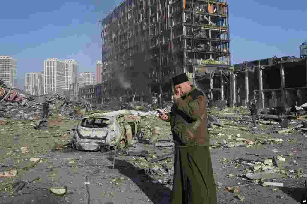 Un sacerdote reza junto a las ruinas de un centro comercial destruido después de un bombardeo, en Kiev, Ucrania, el lunes 21 de marzo de 2022. (Foto AP/Efrem Lukatsky)