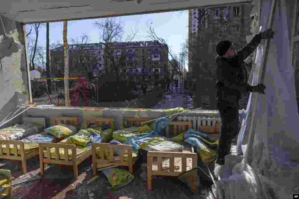 Un hombre quita una cortina destruida dentro de una escuela dañada junto a otros edificios residenciales, en Kiev, Ucrania, el viernes 18 de marzo de 2022. Las fuerzas rusas intensificaron su ataque contra las ciudades ucranianas el viernes, con nuevos ataques con misiles y bombardeos en los bordes de la capital, Kiev, y la ciudad occidental de Lviv, mientras los líderes mundiales presionaban para que se investigaran los repetidos ataques del Kremlin contra objetivos civiles, incluidas escuelas, hospitales y zonas residenciales.&nbsp;