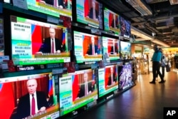 FILE - People stand by TV screens broadcasting the news of Russian troops that have launched their attack on Ukraine, in Hong Kong, Feb. 24, 2022.